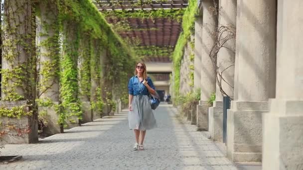 Молода дівчина з рюкзаком, що йде по алеї — стокове відео