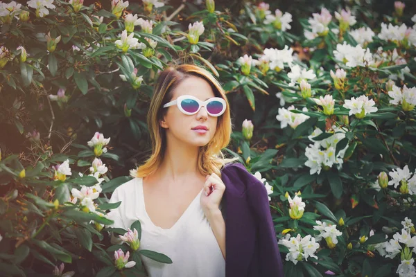 Дівчина в білих сонцезахисних окулярах біля квітів — стокове фото