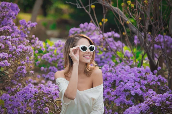 Дівчина в білих сонцезахисних окулярах біля фіолетових квітів — стокове фото