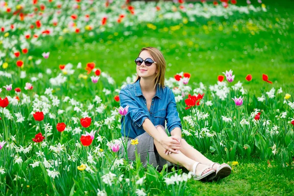 Mladá zrzka dívka sedí na louce tulipány — Stock fotografie