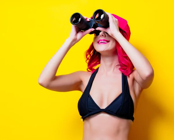 若いピンクのキャップと双眼鏡とビキニの髪の少女 黄色の背景に分離された肖像画 — ストック写真