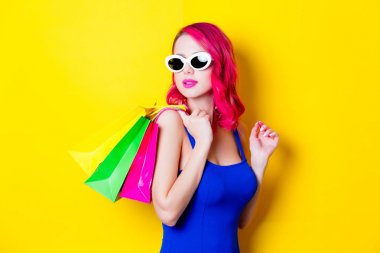 Saç kız renkli alışveriş torbaları ile mavi elbiseli genç pink. Portre sarı arka plan üzerinde izole