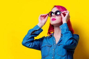 Genç pembe saçlı kız güneş gözlüğü ve mavi gömlek. Portre Sarı zemin üzerine