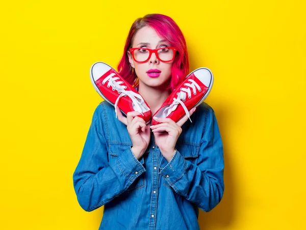 若いピンク髪少女の青いシャツと赤いメガネの願いのための半靴を保持します 黄色の背景に分離された肖像画 — ストック写真