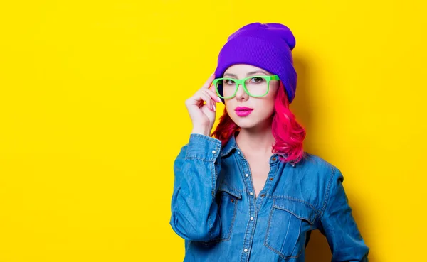 若いピンクの青いシャツ 紫の帽子と緑のメガネで髪の女の子 黄色の背景に分離された肖像画 — ストック写真