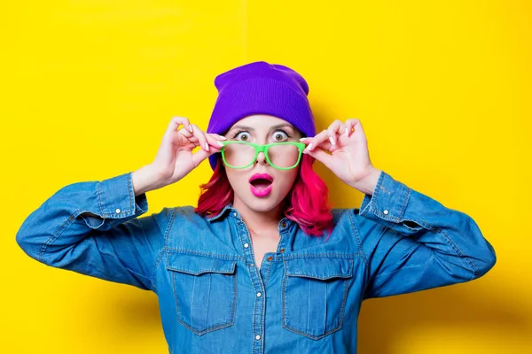若いピンクの青いシャツ 紫の帽子と緑のメガネで髪の女の子 黄色の背景に分離された肖像画 — ストック写真