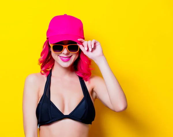 年轻粉红色的头发女孩比基尼和橙色眼镜与帽子 在黄色背景上隔离的肖像 — 图库照片