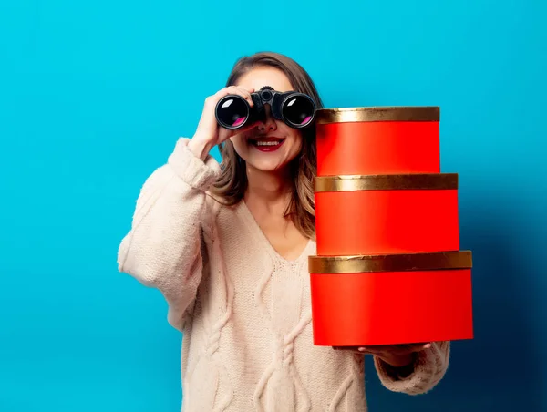 Mooie vrouw met geschenkdoos en verrekijker op blauwe achtergrond — Stockfoto