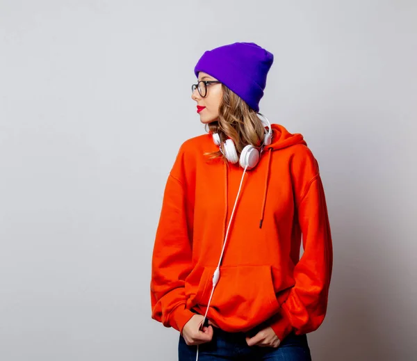 Estilo menina com capuz laranja e chapéu roxo com fones de ouvido — Fotografia de Stock