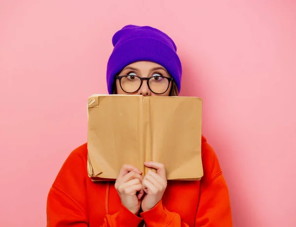 Stijl meisje in oranje hoodie en paarse hoed met boek op roze bac — Stockfoto