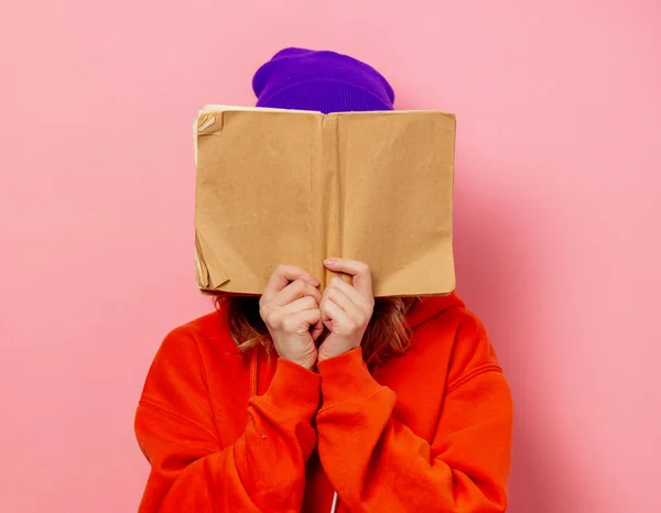 Estilo menina com capuz laranja e chapéu roxo com livro sobre bac rosa — Fotografia de Stock