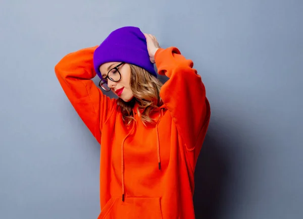 Stile ragazza con cappuccio arancione e cappello viola su sfondo grigio — Foto Stock