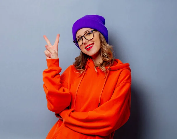 Chica de estilo con capucha naranja y sombrero púrpura sobre fondo gris — Foto de Stock