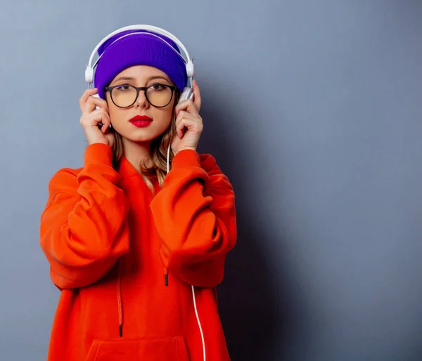 Styl dziewczyna w pomarańczowym kapturze i fioletowy kapelusz ze słuchawkami na gr — Zdjęcie stockowe