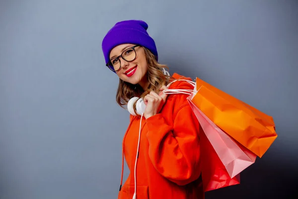 スタイル女の子でオレンジパーカーと紫の帽子でショッピングバッグオン — ストック写真