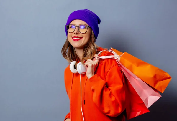 Turuncu kapüşonlu, mor şapkalı, alışveriş çantalı bir kız. — Stok fotoğraf