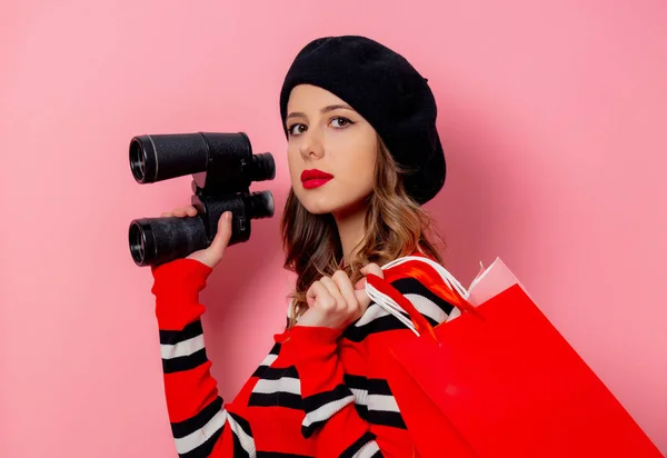 Jovem com binóculos e sacos de compras em fundo rosa — Fotografia de Stock