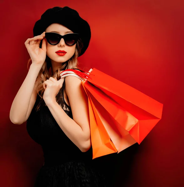 Jeune femme en robe noire avec des sacs à provisions sur fond rouge — Photo