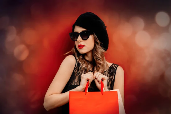 Mujer joven en vestido negro con bolsas de compras sobre fondo rojo —  Fotos de Stock