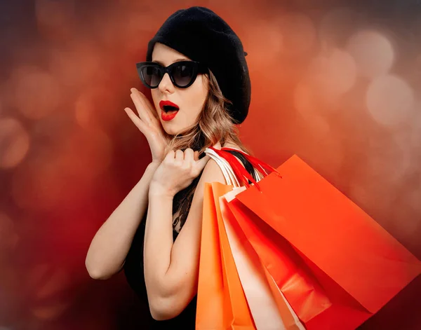 Kırmızı arka planda alışveriş torbaları olan siyah elbiseli genç bir kadın. — Stok fotoğraf