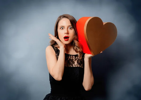 Красива жінка з коробкою у формі серця на сірому фоні з боком — стокове фото