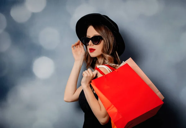 Stijl vrouw in zonnebril met boodschappentassen op grijze achtergrond — Stockfoto