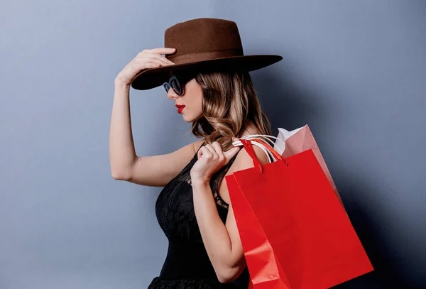 Mujer de estilo en gafas de sol con bolsas de compras sobre fondo gris —  Fotos de Stock