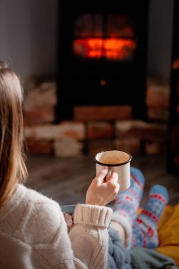 Evdeki şöminenin yanında elinde bir fincan kahve olan kız.