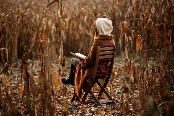 Estilo mujer con libro sentado en silla en el campo de maíz en otoño t — Foto de Stock