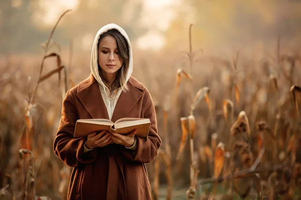 Стильная женщина с книгой о кукурузном поле в осенний сезон — стоковое фото