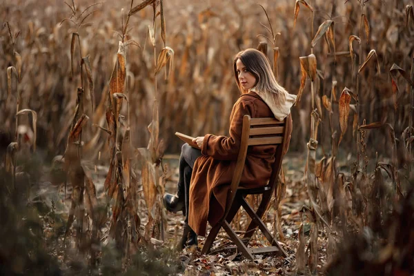 Stylowa kobieta z książki siedzi na krześle na polu kukurydzy jesienią t — Zdjęcie stockowe