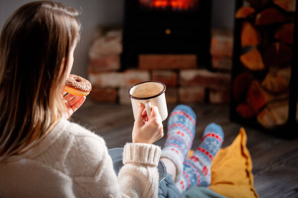 girl with a cup of coffee and donuts by the fireplace at home