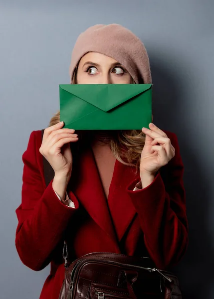 Jeune femme facteur avec enveloppe verte sur fond gris — Photo