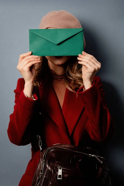 Young woman postman with green envelope on grey background — Stock Photo, Image