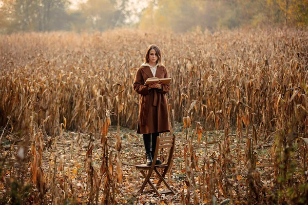 Stijl vrouw met boek verblijf op stoel op maïsveld in de herfst tijd — Stockfoto