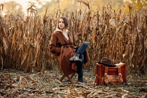 Mujer de estilo con maleta sentada en silla en el campo de maíz en autu —  Fotos de Stock