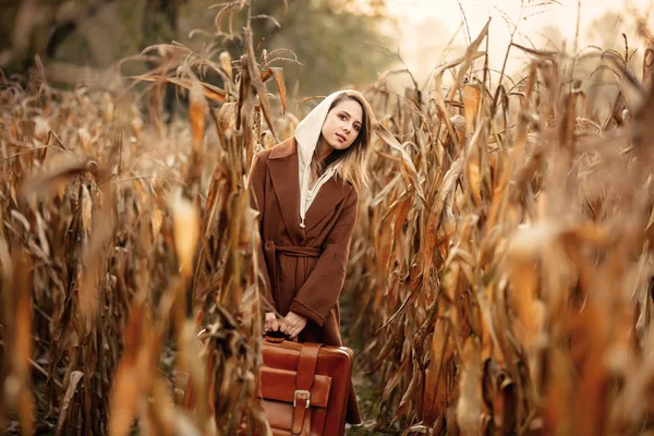 Frau im Mantel mit Koffer auf Maisfeld im Herbst — Stockfoto