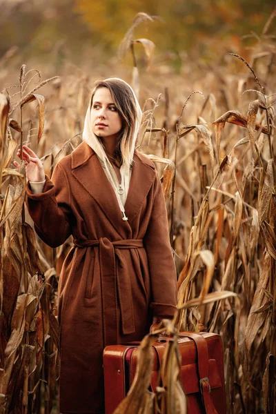 Stylowa kobieta w płaszczu z walizką na polu kukurydzy w czasie jesieni s — Zdjęcie stockowe