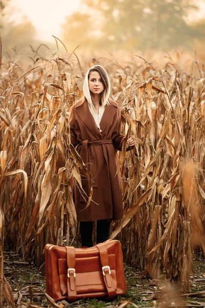 Stijl vrouw in jas met koffer op maïsveld in de herfst tijd s — Stockfoto