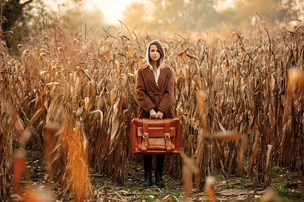 Stijl vrouw in jas met koffer op maïsveld in de herfst tijd s — Stockfoto