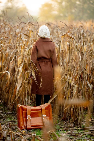 Stílus nő kabátban bőrönddel kukoricamezőn ősszel s — Stock Fotó