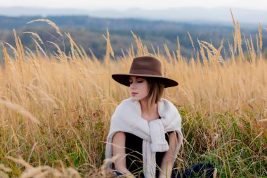 Süveter giyen stil kızı kırsal kesimde sarı çimenlerde benimle oturuyor.