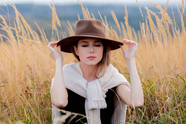 스웨터를 입은 스타일의 아가씨는 시골의 노란색 잔디에 앉아 있습니다. — 스톡 사진