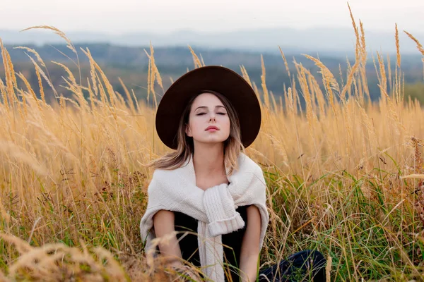 Chica de estilo en suéter se sienta en la hierba amarilla en el campo con m — Foto de Stock