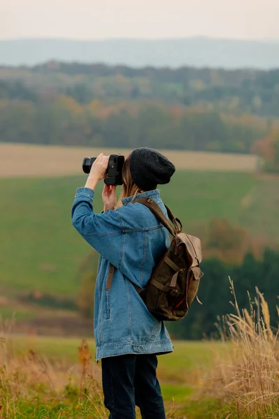 Styl dívka s kamerou a batohem na venkově s horou — Stock fotografie