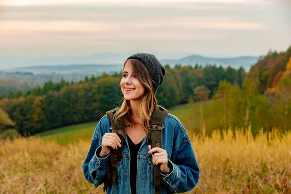 Stil fată în jachetă de denim și pălărie cu rucsac în mediul rural — Fotografie, imagine de stoc