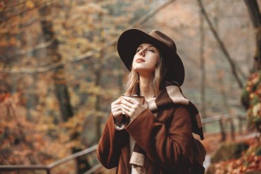 Sonbahar sezonu parkında elinde kahve olan genç bir kadın.