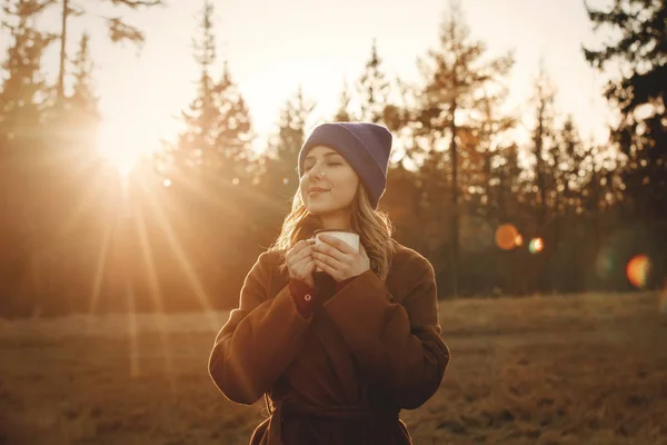 Jovem com xícara de café ficar perto de madeira ao pôr do sol — Fotografia de Stock