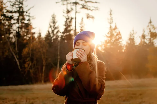 Молодая женщина с чашкой кофе оставаться рядом с лесом в закатное время — стоковое фото