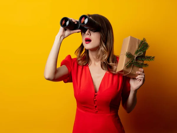 Schöne Frau Mit Geschenkbox Und Fernglas Auf Gelbem Hintergrund — Stockfoto